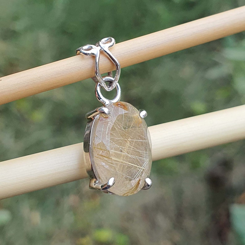 May include: Silver pendant featuring a clear quartz stone with gold inclusions. The stone is oval shaped and set in a silver bezel.