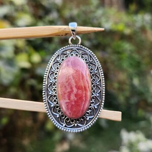 Pode incluir: Um pingente de prata com uma gema oval rosa e branca engastada em um design filigranado.