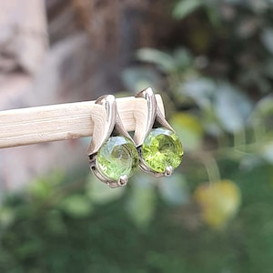 May include: A pair of silver earrings with green gemstone accents. The earrings are in the shape of a teardrop with a round gemstone in the center.