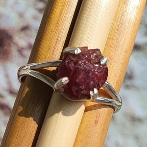 Puede incluir: Un anillo de plata con una piedra preciosa de rub&iacute; rojo en bruto. El rub&iacute; est&aacute; engastado en un dise&ntilde;o simple y moderno.
