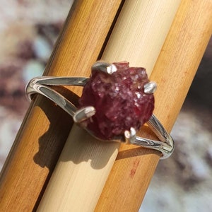 Puede incluir: Un anillo de plata con una piedra preciosa de rub&iacute; rojo en bruto engastada en el centro. El rub&iacute; es de color rojo intenso y tiene una textura rugosa y natural.