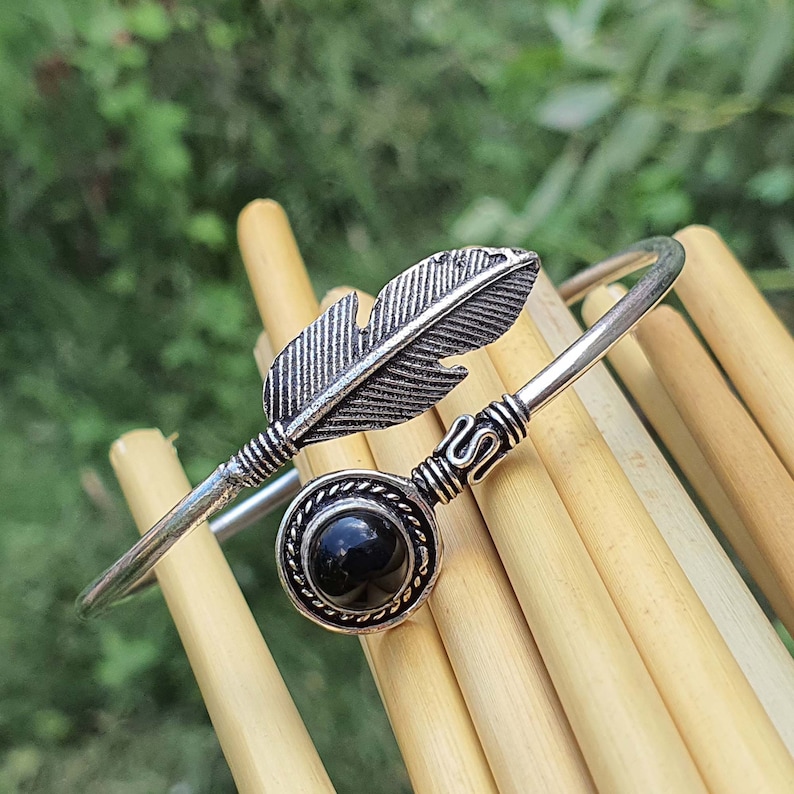 Op de afbeelding: Zilveren armband met een zwarte steen en een veren ontwerp.