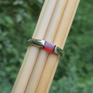May include: A silver ring with a rectangular red gemstone.