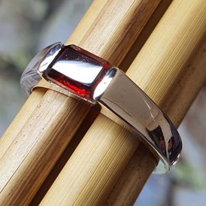 May include: A silver ring with a rectangular red gemstone.