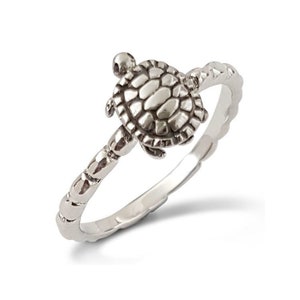 Puede incluir: Un anillo de plata con un diseño de tortuga detallado. La banda está texturizada con un patrón de cuentas.