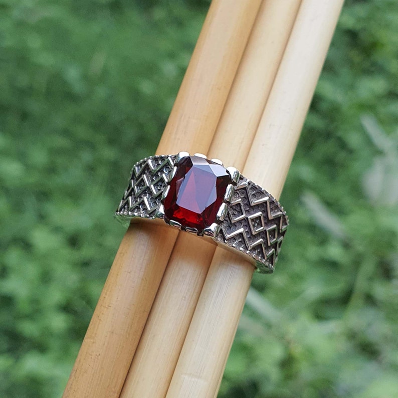 May include: A silver ring with a red gemstone set in a geometric pattern.