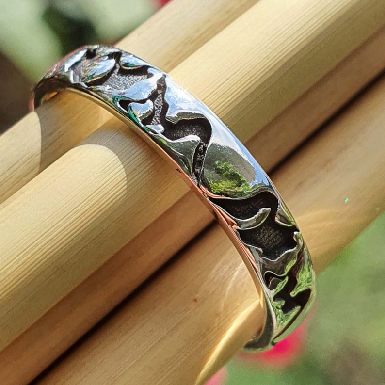 May include: A silver ring with a textured design of mountains and valleys. The ring is shown on a wooden surface.