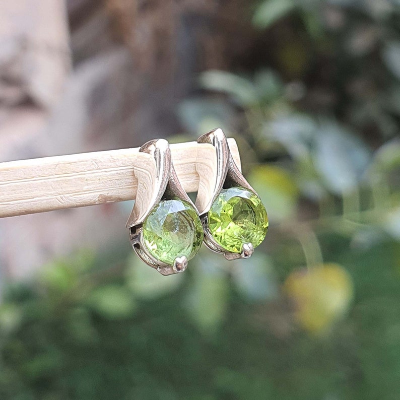 May include: A pair of silver earrings with green gemstone accents. The earrings are in the shape of a teardrop with a round gemstone in the center.