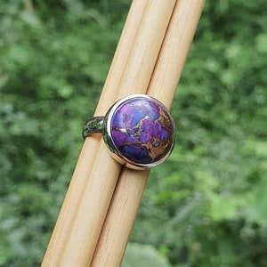 May include: A silver ring with a round purple and gold gemstone. The gemstone has a marbled pattern.