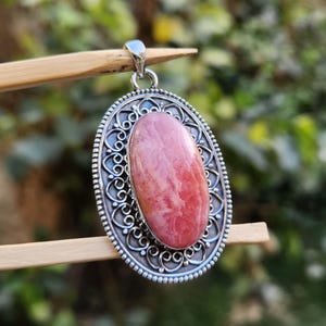 Pode incluir: Um pingente de prata com uma gema oval rosa e branca engastada em um design filigranado.