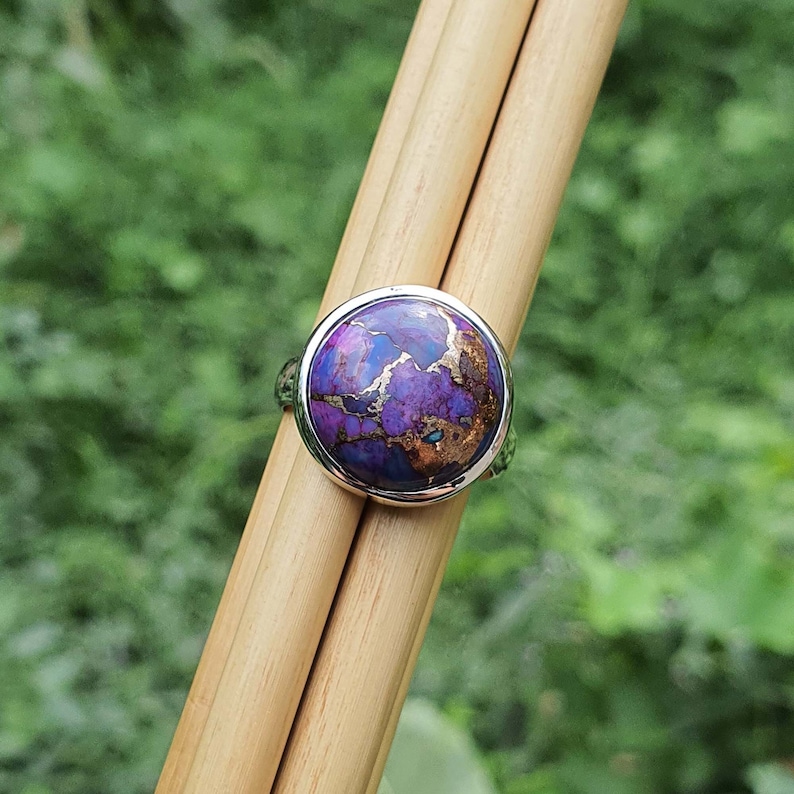 May include: A silver ring with a round purple and copper gemstone set in a bezel setting.