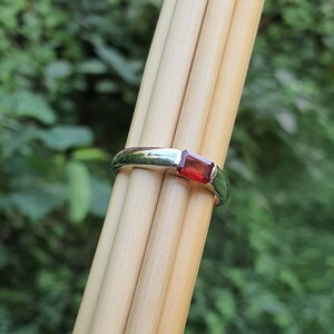 May include: A silver ring with a rectangular red gemstone.