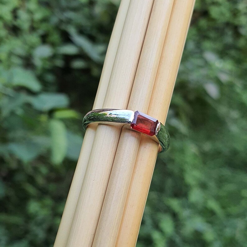 May include: A silver ring with a rectangular red gemstone.