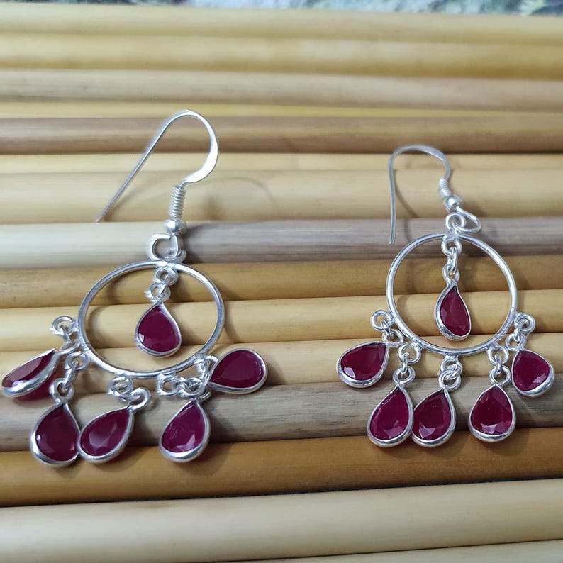 May include: Silver dangle earrings with a circular hoop and multiple teardrop-shaped red gemstones.