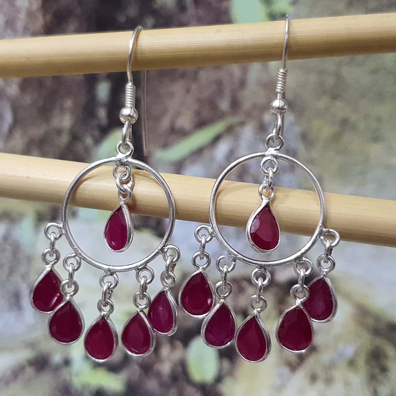 May include: Silver dangle earrings with a circular design and multiple teardrop-shaped red gemstones.