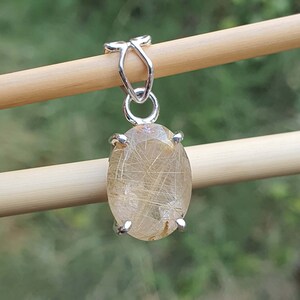May include: A silver pendant featuring a clear oval-shaped gemstone with gold inclusions. The pendant is suspended from a silver bail.