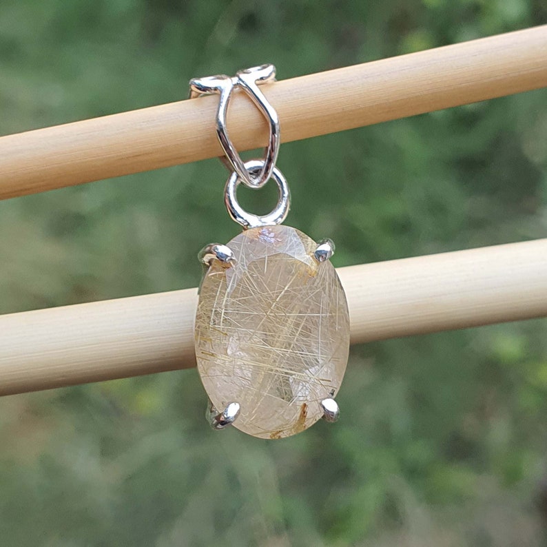 May include: A silver pendant featuring a clear oval-shaped gemstone with gold inclusions. The pendant is suspended from a silver bail.