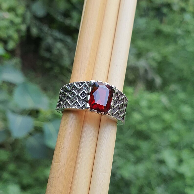 May include: A silver ring with a red gemstone set in a geometric pattern.