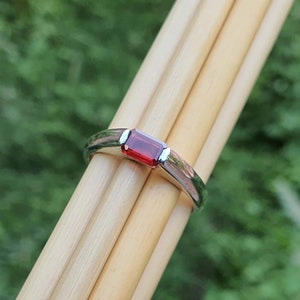 May include: A silver ring with a rectangular red gemstone set in the centre.