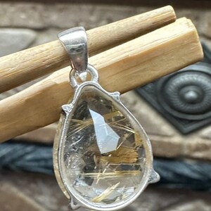 May include: Silver pendant featuring a teardrop-shaped clear quartz crystal with gold inclusions. The pendant is approximately 1 inch in length.