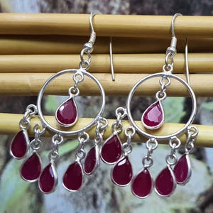 May include: A pair of silver dangle earrings with a circular design and multiple teardrop-shaped red gemstones.