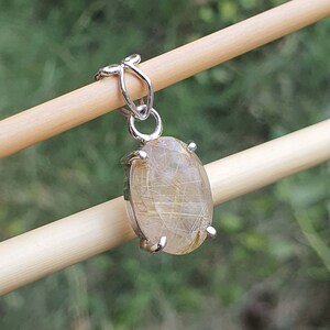 May include: A silver pendant featuring a clear quartz crystal with gold inclusions. The crystal is oval shaped and set in a silver bezel.