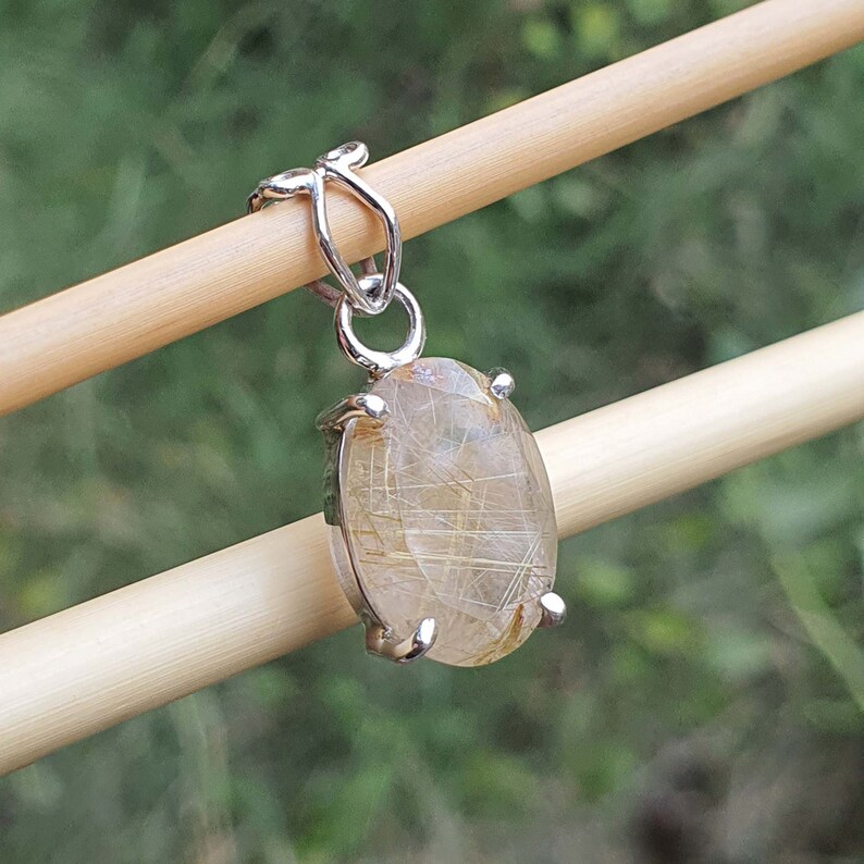 May include: A silver pendant featuring a clear quartz crystal with gold inclusions. The crystal is oval shaped and set in a silver bezel.