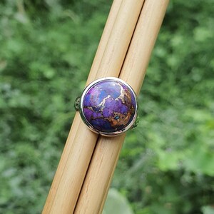 May include: A silver ring with a round purple and copper gemstone set in a bezel setting.