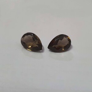 May include: Two pear-shaped, brown gemstones with a faceted cut. The gemstones are set against a white background.