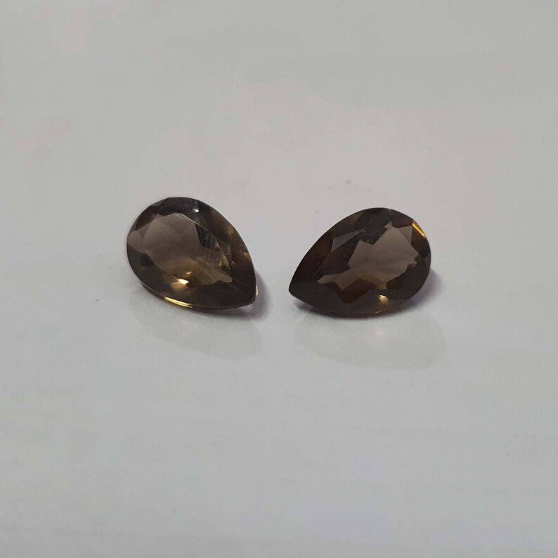 May include: Two pear-shaped, brown gemstones with a faceted cut. The gemstones are set against a white background.