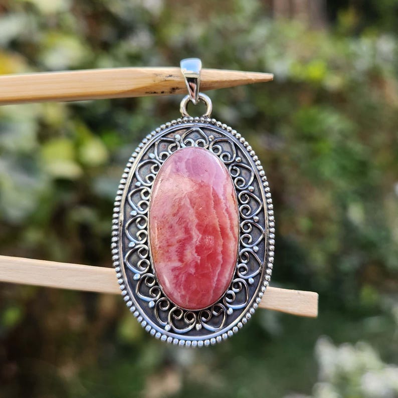 Pode incluir: Um pingente de prata com uma gema oval rosa e branca engastada em um design filigranado.