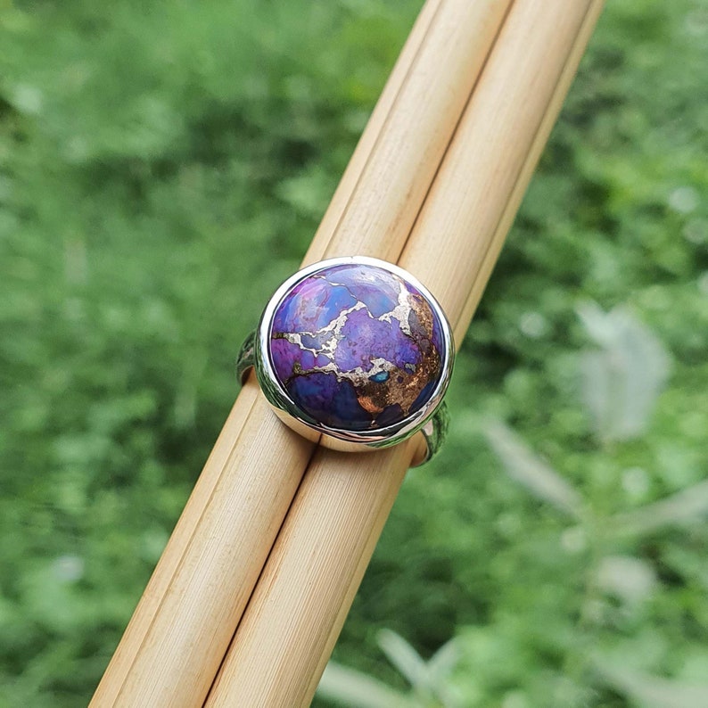 May include: A silver ring with a round purple and copper turquoise stone.