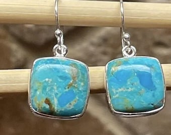 May include: A pair of square turquoise earrings with a silver-colored border. The turquoise stones have a mottled pattern of blue and brown. The earrings hang from a simple hook.