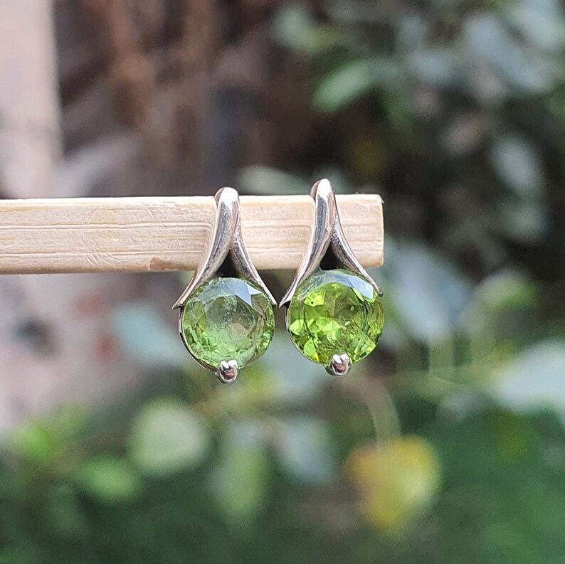 May include: A pair of silver earrings with green gemstone accents. The earrings have a delicate, curved design and feature round, faceted gemstones.