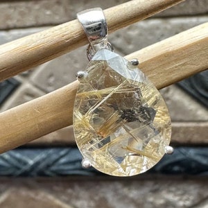 May include: A silver pendant featuring a teardrop-shaped clear quartz crystal with gold inclusions. The crystal is set in a silver bezel and has a silver bail.