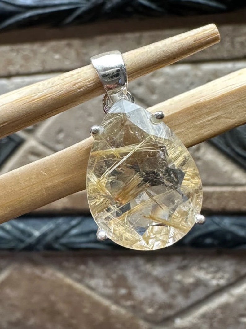 May include: A silver pendant featuring a teardrop-shaped clear quartz crystal with gold inclusions. The crystal is set in a silver bezel and has a silver bail.