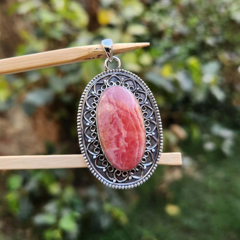 Pode incluir: Um pingente de prata com uma gema oval rosa e branca engastada em um design filigranado.