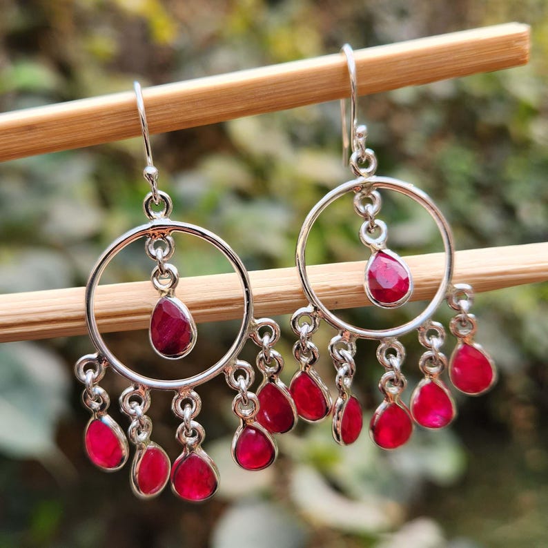 May include: A pair of silver hoop earrings with dangling red gemstone drops. The earrings have a circular design with multiple smaller circles hanging from the bottom.