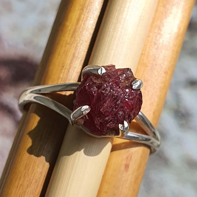 Puede incluir: Un anillo de plata con una piedra preciosa de rub&iacute; rojo en bruto. El rub&iacute; est&aacute; engastado en garras y tiene un aspecto &aacute;spero y natural.