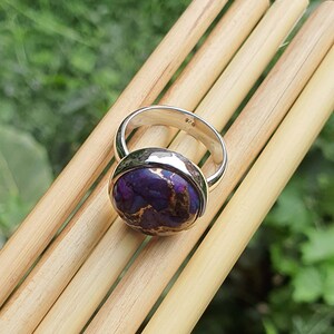 May include: A silver ring with a purple and copper turquoise stone. The ring is marked 925, indicating it is made of sterling silver.