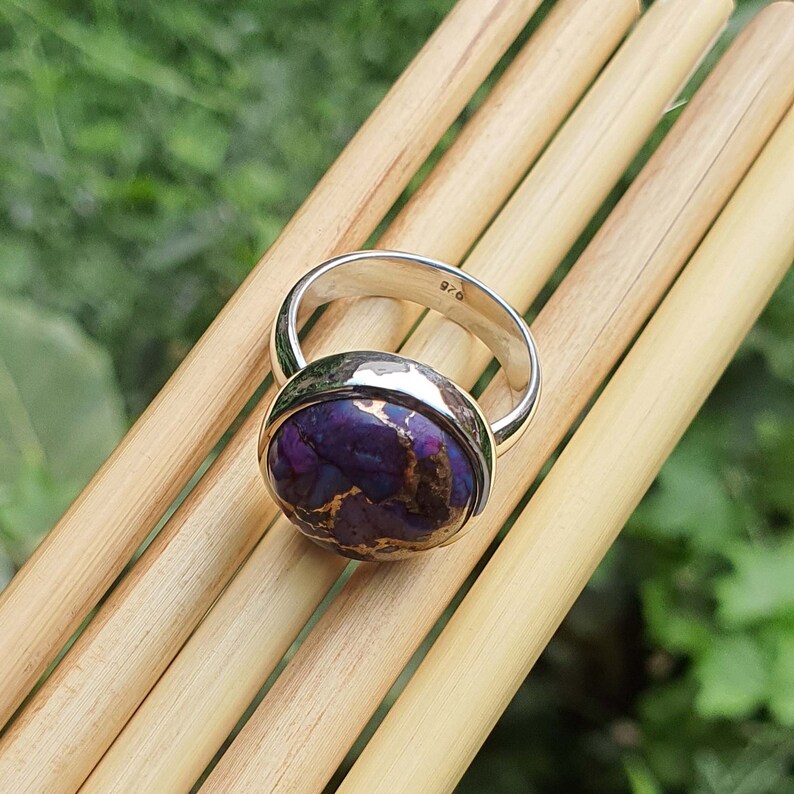 May include: A silver ring with a purple and copper turquoise stone. The ring is marked 925, indicating it is made of sterling silver.