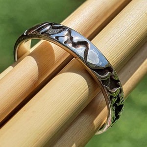 May include: A silver ring with a textured design. The ring is on a wooden surface.