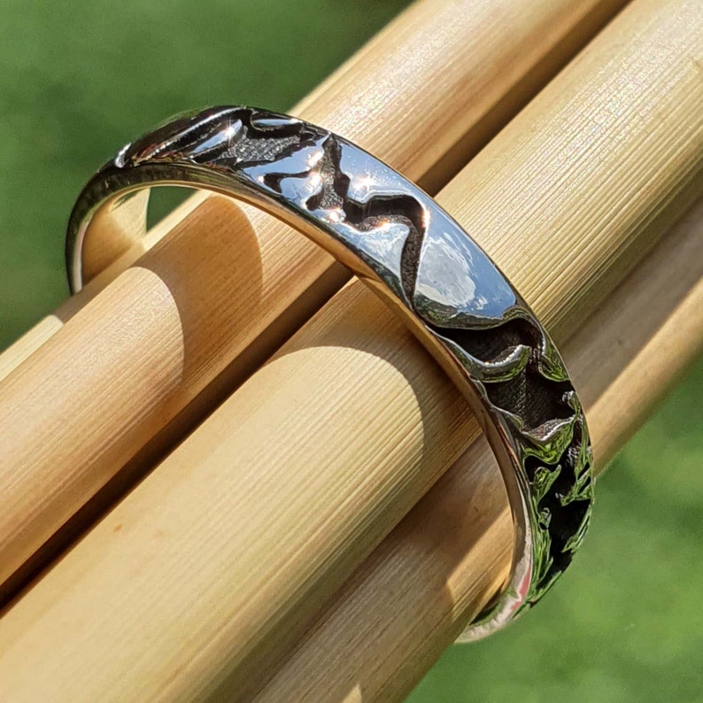 May include: A silver ring with a textured design. The ring is on a wooden surface.