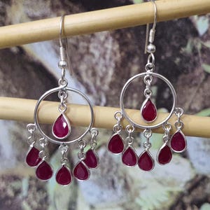 May include: Silver dangle earrings with a circle design and multiple teardrop-shaped red gemstones.