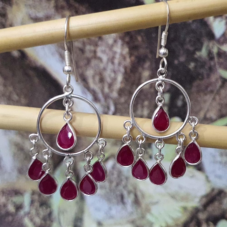 May include: Silver dangle earrings with a circle design and multiple teardrop-shaped red gemstones.