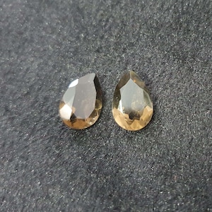 May include: Two teardrop-shaped, faceted gemstones. The gemstones are a light brown color with a slight golden hue.
