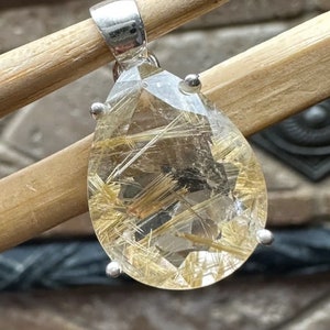 May include: A silver pendant featuring a clear quartz crystal with gold inclusions. The crystal is faceted and has a teardrop shape.