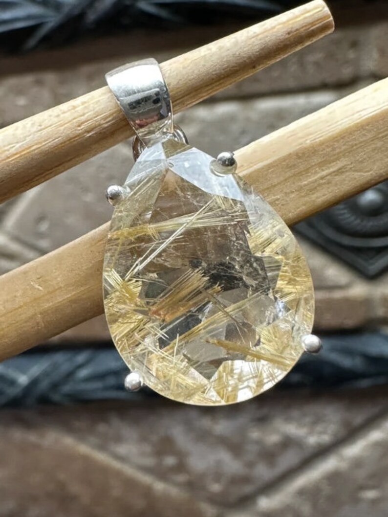 May include: A silver pendant featuring a clear quartz crystal with gold inclusions. The crystal is faceted and has a teardrop shape.