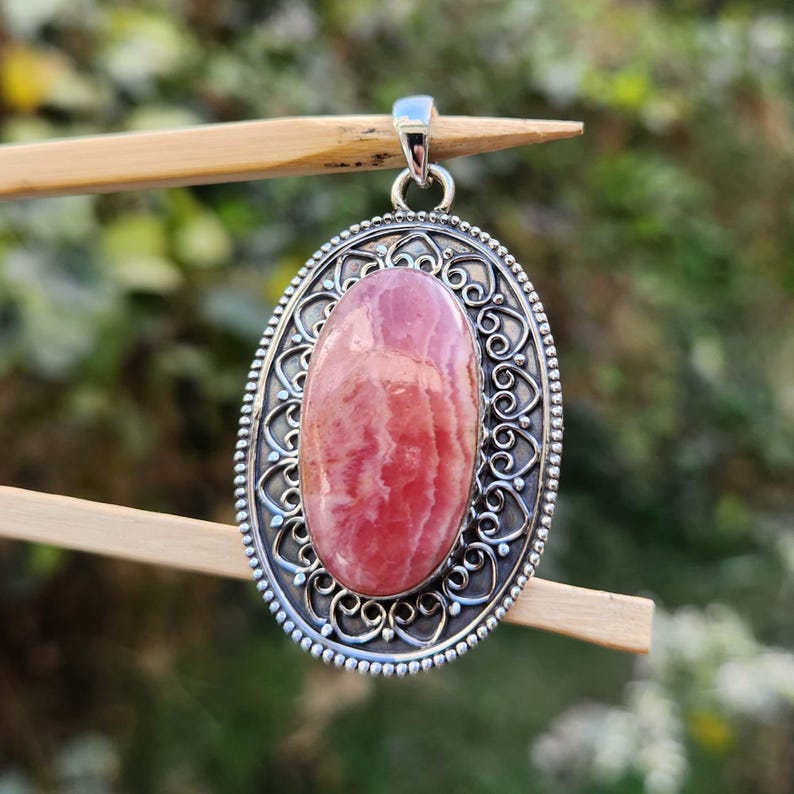 Pode incluir: Um pingente de prata com uma gema oval rosa e branca engastada em um design filigranado.