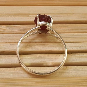 Puede incluir: Un anillo de plata con una piedra preciosa roja engastada en garras. El anillo est&aacute; sobre una superficie de madera.